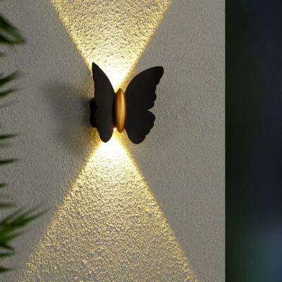 Applique murale extérieure farfalla noir corps doré allumée mur blanc quelques feuilles vertes