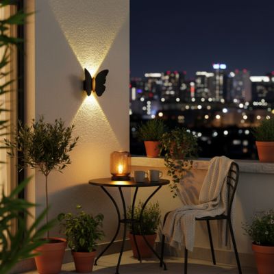 Applique murale extérieure papillon ailes noires corps doté mur balcon table chaise jeté plantes vue sur ville la nuit