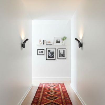Applique murale noire courbe halo lumineux vers le haut couloir moderne éclectique minimaliste tout blanc tapis kilim couleurs vives