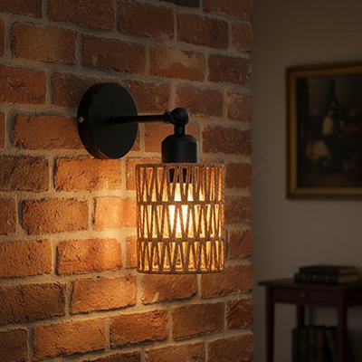 Applique murale rotin bohème noire avec abat-jour cylindrique tressé installée sur mur brique diffusant lumière chaude