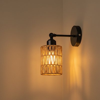 Applique murale rotin bohème noire avec abat-jour cylindrique tressé diffusant lumière chaude sur mur beige