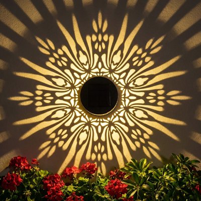 Éclairage extérieur mural LED solaire motif mandala doré projetant ombres décoratives rayonnantes sur mur avec fleurs rouges