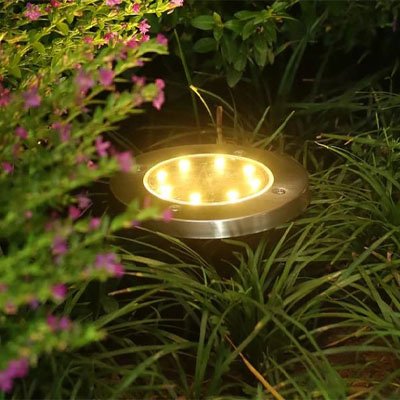 Eclairage exterieur solaire disque acier inoxydable allumée une lampe en premier plan dans l'herbe