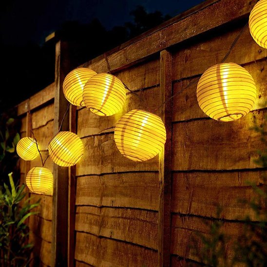 Guirlande solaire lanternes rondes dorées suspendues clôture bois jardin nuit, lumière chaude ambrée