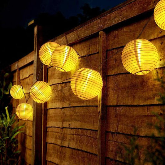Guirlande solaire lanternes rondes dorées suspendues clôture bois jardin nuit, lumière chaude ambrée