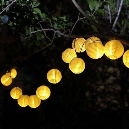 Guirlande solaire lanternes LED rondes dorées suspendues branches arbres nuit fond noir, ligne lanternes lumière chaude