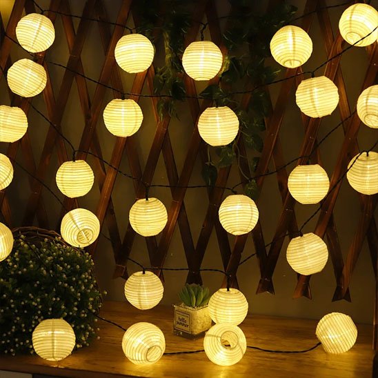 Guirlande solaire lanternes rondes blanches dorées suspendues treillis bois terrasse nuit, multiples lanternes lumière