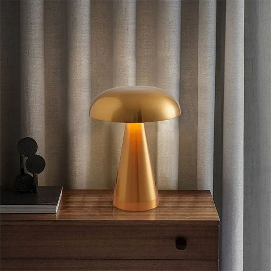 lampe champignon dorée métal sur bureau en bois livre derrière des rideaux gris fermés rechargeable 3 ambiances