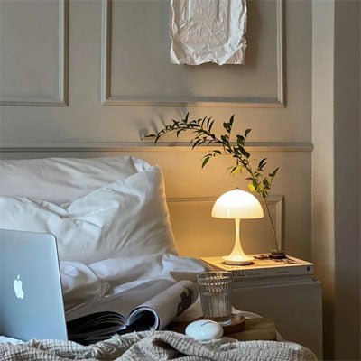 lampe champignon blanche allumée sur table de nuit blanche lit blanc ordinateur et revue ambiance sereine