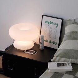 Lampe champignon blanche en verre posée sur une table de chevet noire
