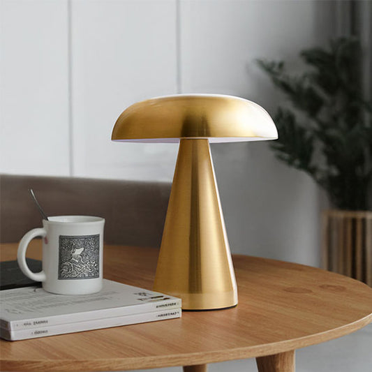 lampe champignon dorée métal sur table en bois une tasse sur un livre dans coin au fond une plante verte