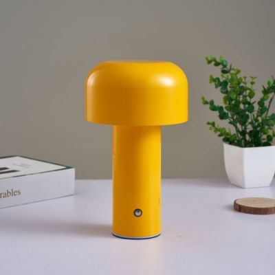 lampe champignon jaune sur table blanche un livre et petite plante dans pot blanc