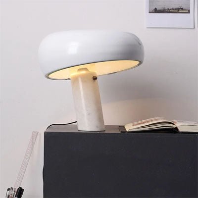 lampe champignon pied marbre blanc abat-jour blanc allumée sur table noire un livre ouvert