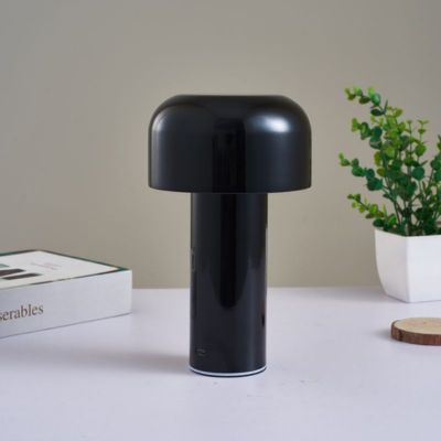 lampe champignon noire sur table blanche un livre et petite plante dans pot blanc