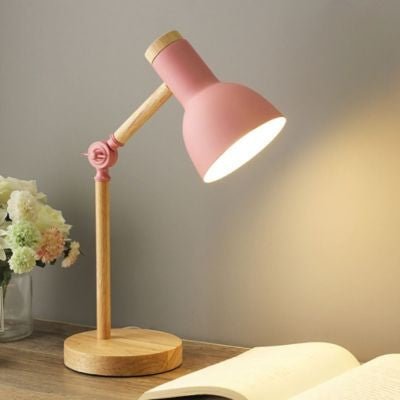 lampe de bureau rose poudre avec base bois et bras articulé allumée sur table de chevet avec livre ouvert et vase fleurs blanches