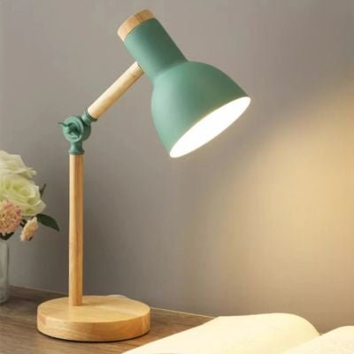 lampe de bureau vert menthe avec base bois et bras articulé allumée sur table de chevet avec livre ouvert et vase fleurs blanches