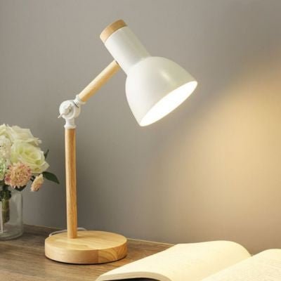 lampe de bureau blanche avec base bois et bras articulé allumée sur table de chevet avec livre ouvert et vase fleurs blanches