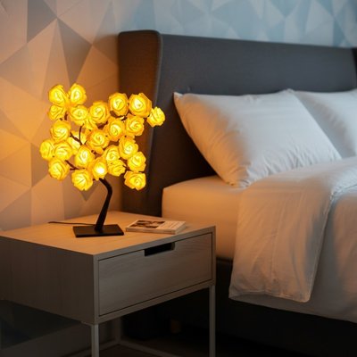 Lampe de chevet design forme arbre fleurs jaunes allumées base noire sur table de nuit en bois style nordique
