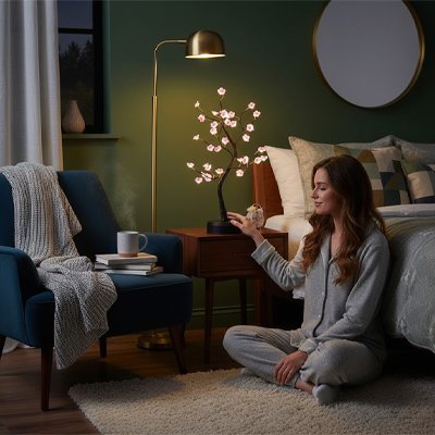 Lampe de chevet design forme de bonsaï fleurs rose dans chambre style nordique jeune femme assise sol en pyjama