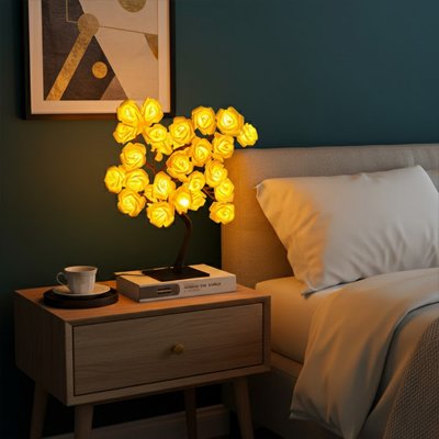 Lampe de chevet design forme arbre pied noir roses jaunes allumées sur table de nuit en bois dans ambiance nordique
