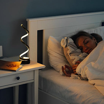 lampe de chevet spirale noire sur une table de nuit une femme dort dans des draps blancs