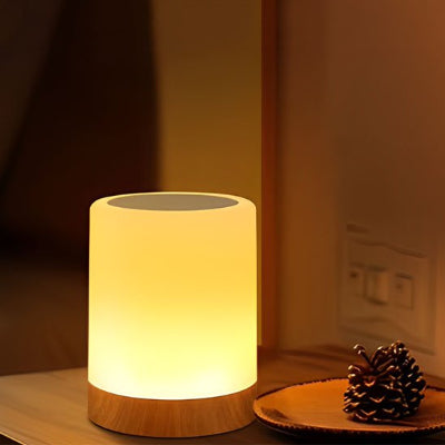 Lampe de chevet tactile allumée dans pénombre sur table bois assiette et cocotte de pin