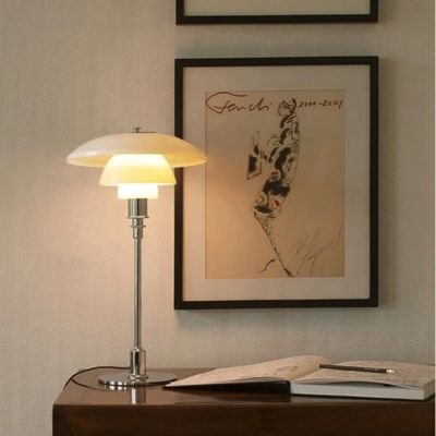 lampe de table danoise allumée sur crédence bois foncé un livre ouvert crayon et cadre au mur