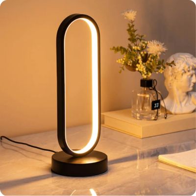 lampe de table noire allumée, forme de cercle allongé, minimaliste futuriste LED dix intensités trois modes d'éclairage sur table blanche fleurs séchées buste antique blanc  livre  
