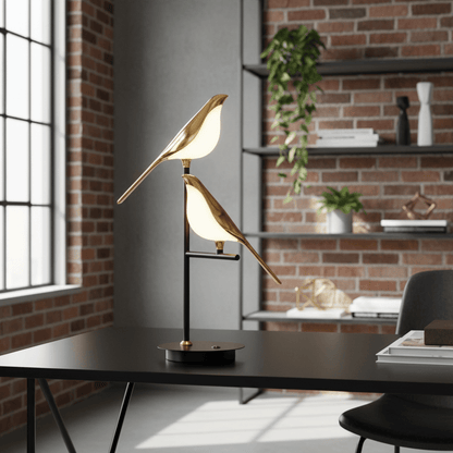 lampe de table led tricolore doux oiseaux blancs aux ailes dorées perchés sur une branche en fer traité dans style moderne industriel murs briques table noire étagères métal