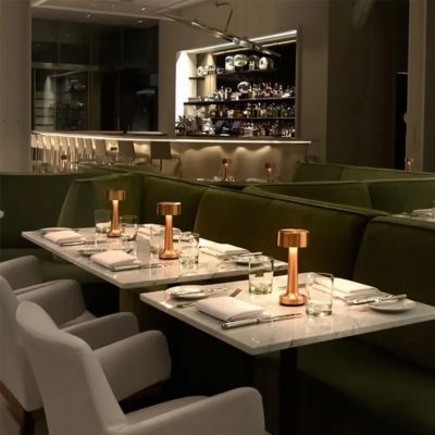 lampe de table portable dorée posée chacune sur table restaurant les tables couverts montées banquettes vert olive chaises gris pâle 