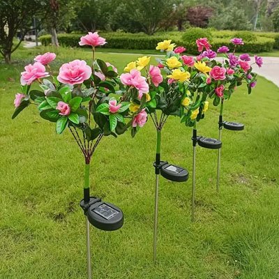 Lampe solaire extérieur décoratives fleurs roses jaunes violettes sur tiges plantées dans pelouse jardin ensoleillé