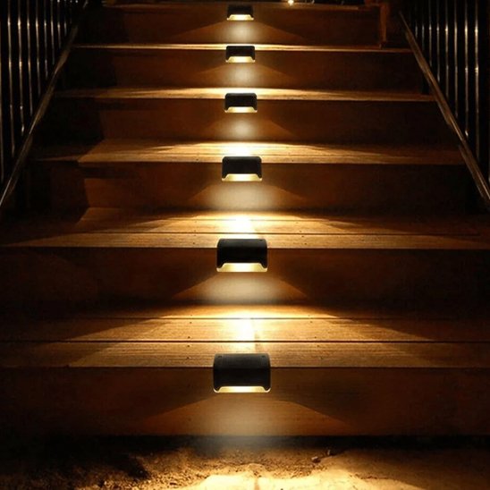 Lampe solaire veilleur nocturne noire murale noire installée sur escalier en bois diffusant lumière chaude vers le bas