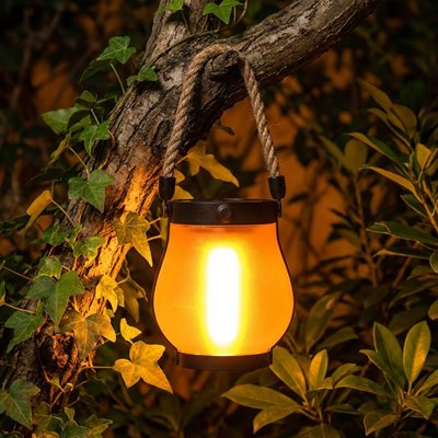 Lanterne exterieur solaire effet flamme orange vif anse corde suspendue branche nuit, lierre feuillage vert éclairé lumière chaude 
