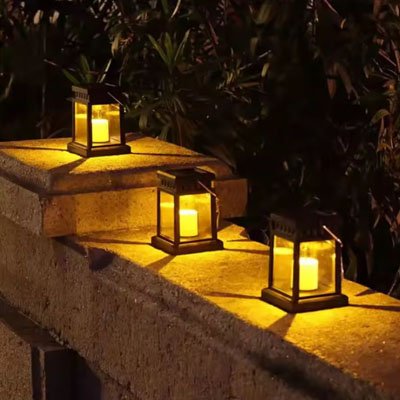 Lanterne solaire dorée trois sont alignées sur muret pierre nuit, végétation sombre fond, lumière chaude ambre, décoration t