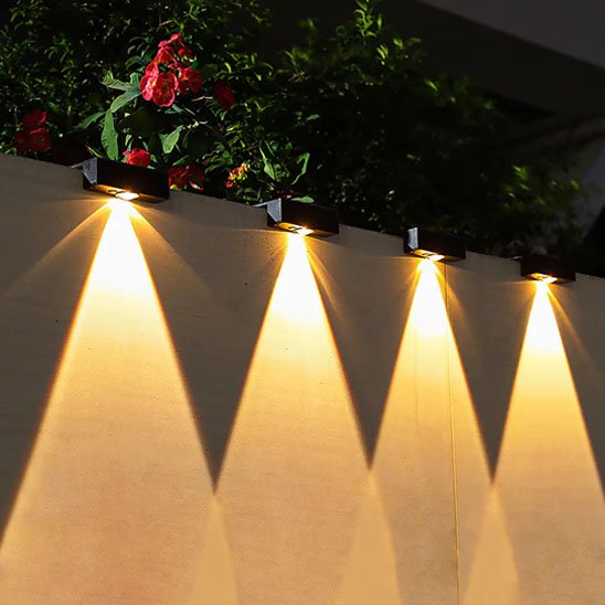 Luminaire extérieur lampes solaires murales noires alignées sur clôture jardin avec fleurs rouges diffusant lumière chaude triangulaire vers le bas