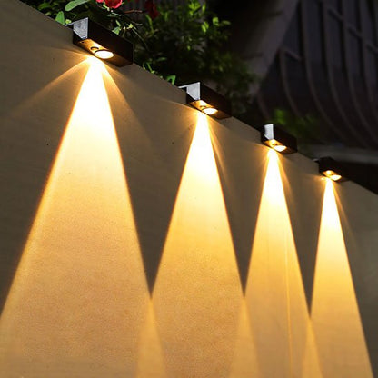 Luminaire extérieur murale noires alignées sur clôture extérieure diffusant lumière chaude triangulaire vers le bas